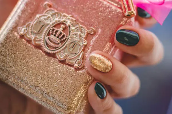 Woman holding a glitter covered perfume bottle with glittery, manicured nails.