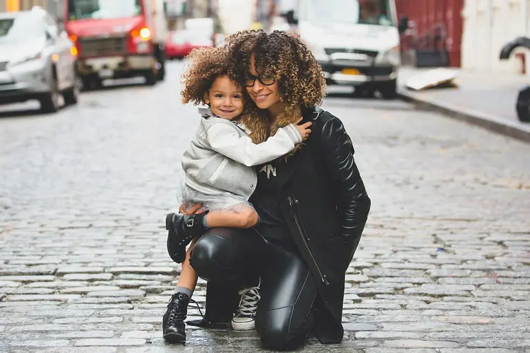 Stylish mixed-race woman hugging her daughter. with street in the background